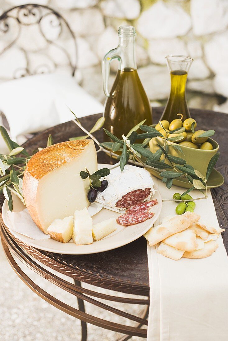 Käse, Salami, Oliven, Olivenöl, Cracker auf Tisch im Freien