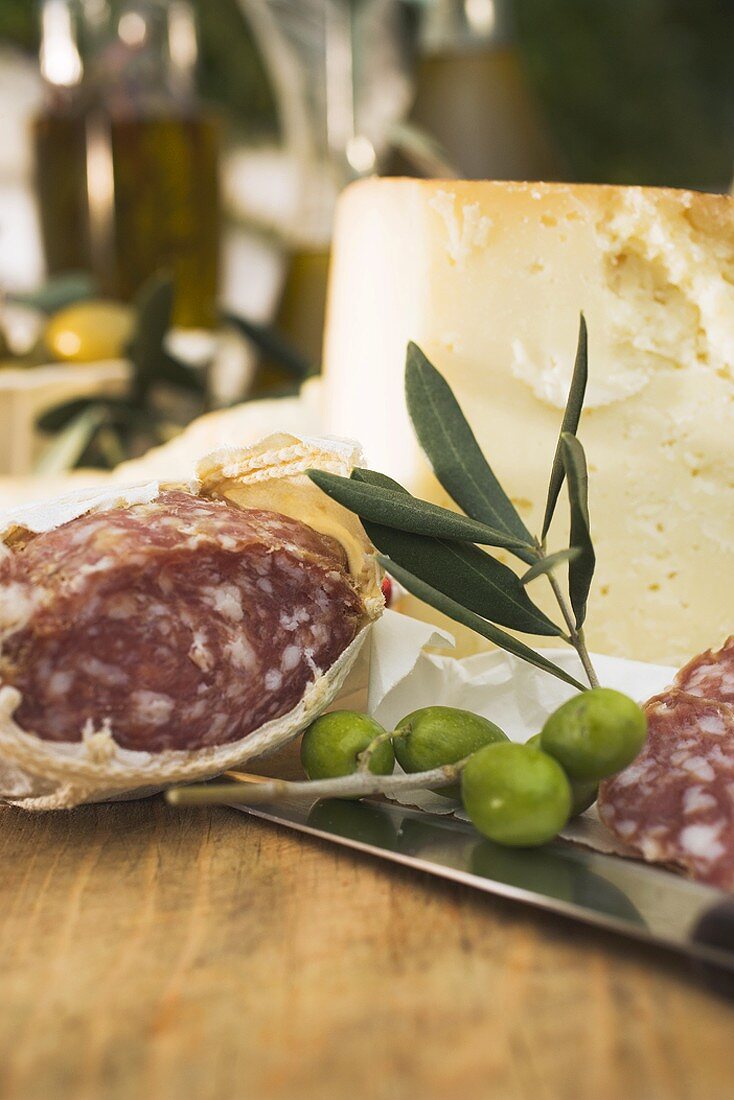 Salami, green olives and cheese on table