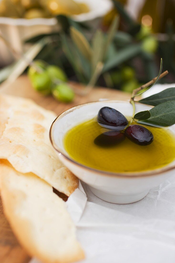 Olivenöl im Schälchen mit schwarzen Oliven, daneben Cracker