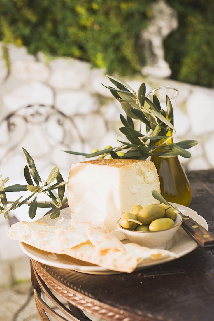 Cheese, green olives, crackers & olive oil on outdoor table