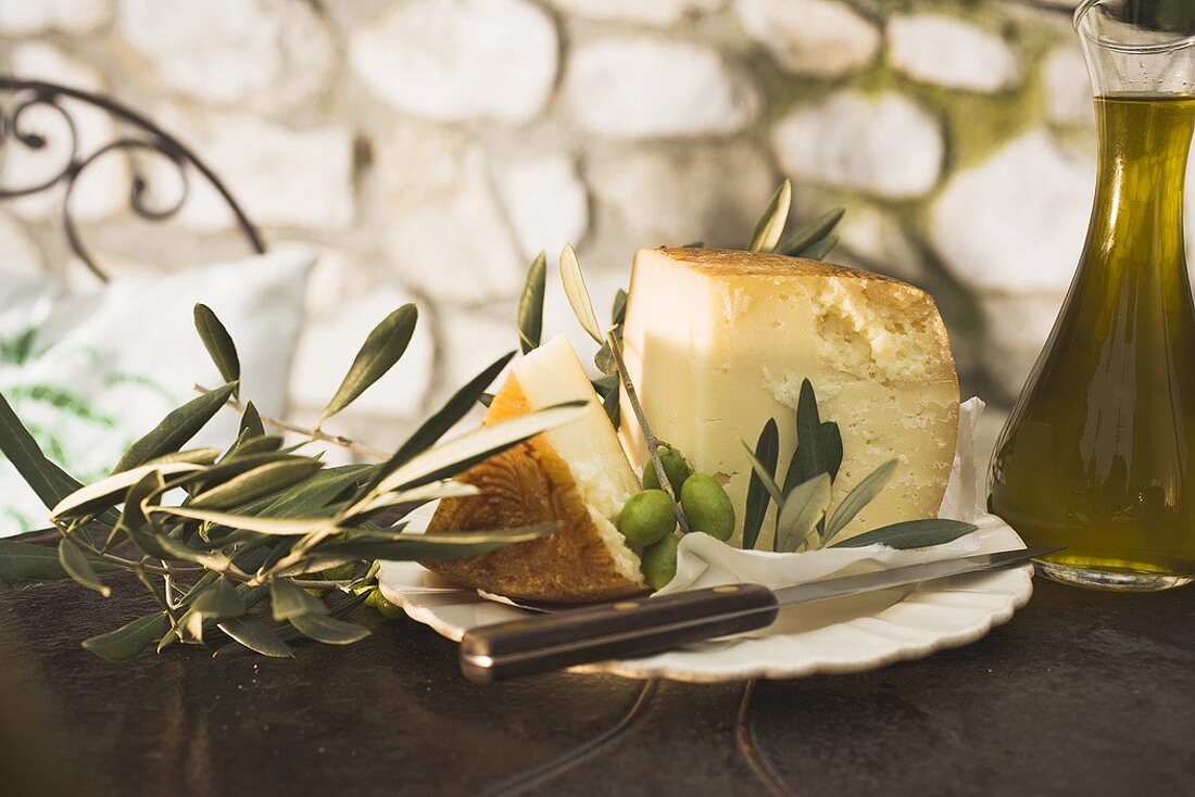 Käse, grüne Oliven und Olivenöl auf Tisch im Freien