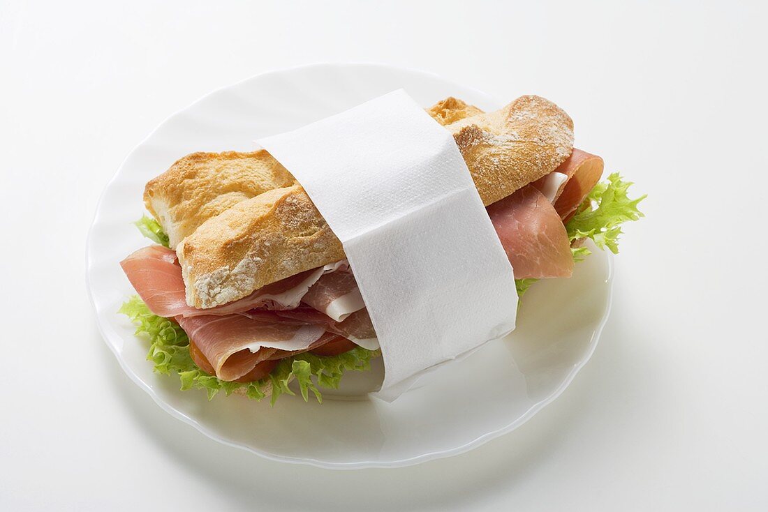 Sandwich mit Rohschinken in Papierserviette auf Teller