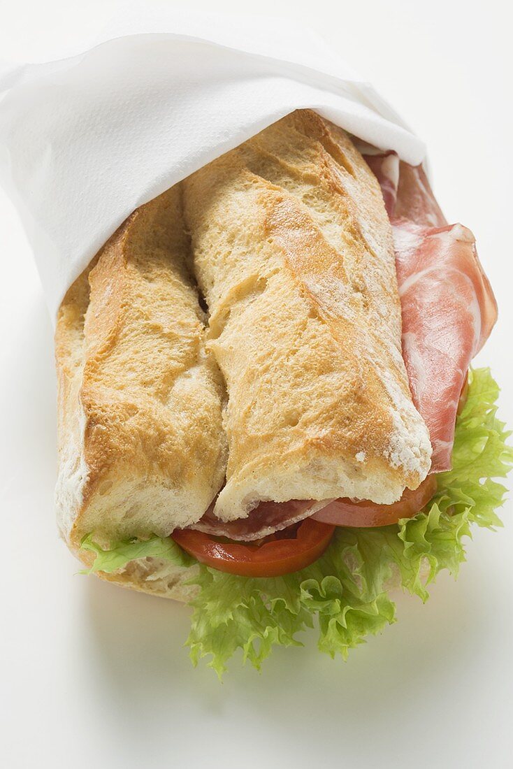 Sandwich mit Wurst, Tomaten und Salatblatt in Papierserviette