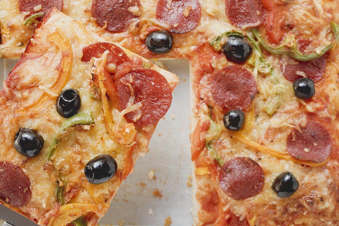 Pizza mit Peperoniwurst, Paprika und Oliven (angeschnitten)