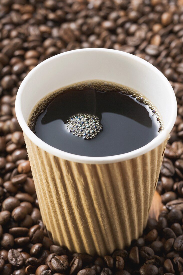 Black coffee in paper cup on coffee beans