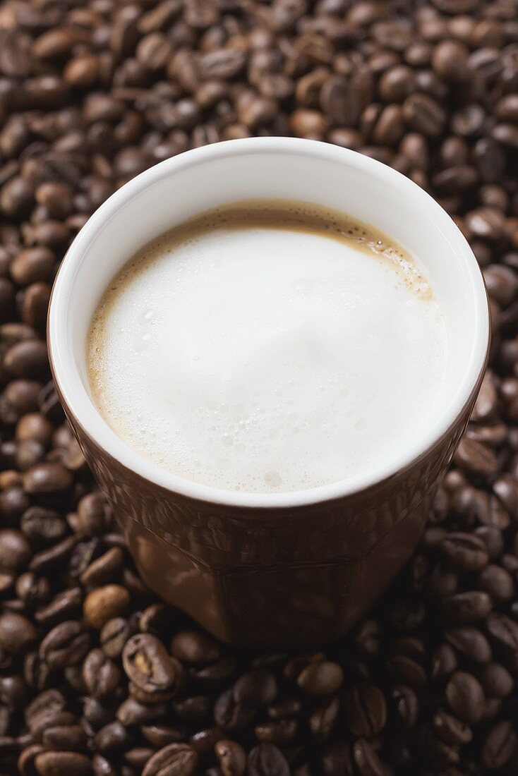 Tasse Kaffee mit Milchschaum auf Kaffeebohnen