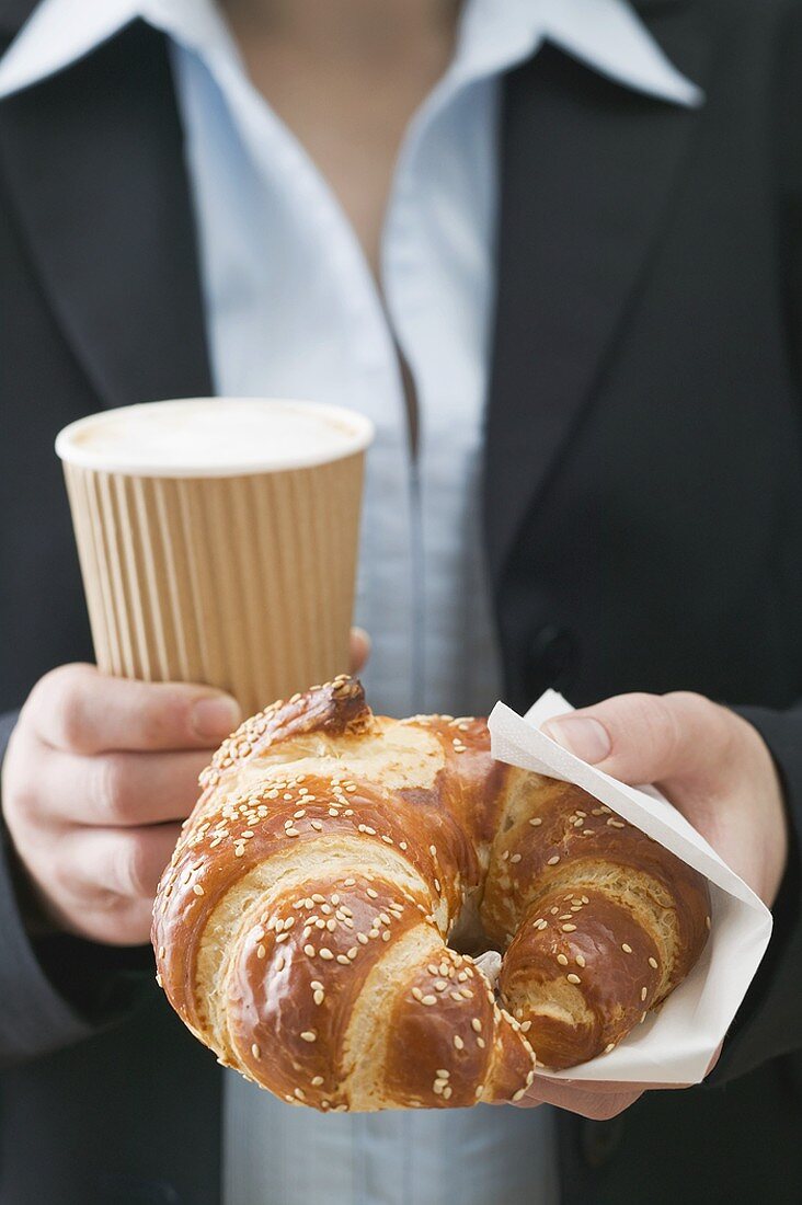 Woman holding pretzel-style croissant & coffee in plastic cup