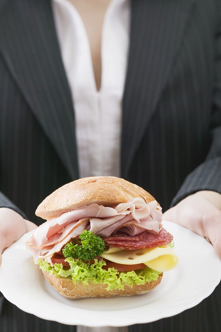 Frau hält Schinken-Käse-Sandwich auf Teller