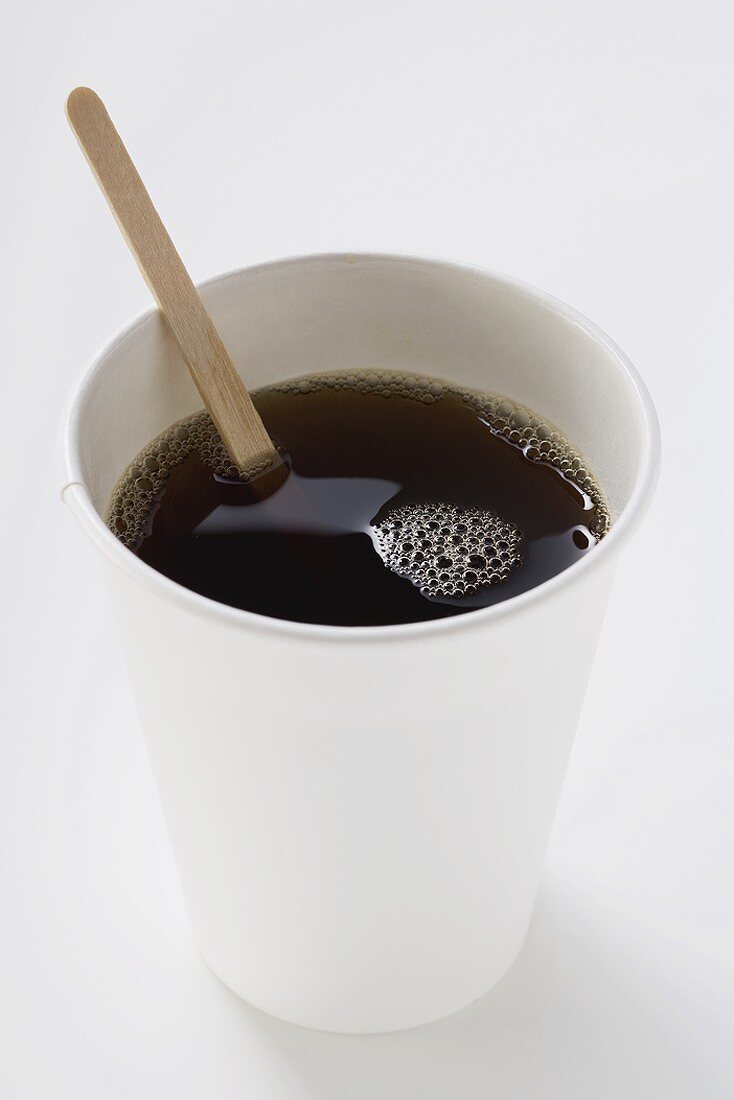 Black coffee in paper cup with wooden stirrer