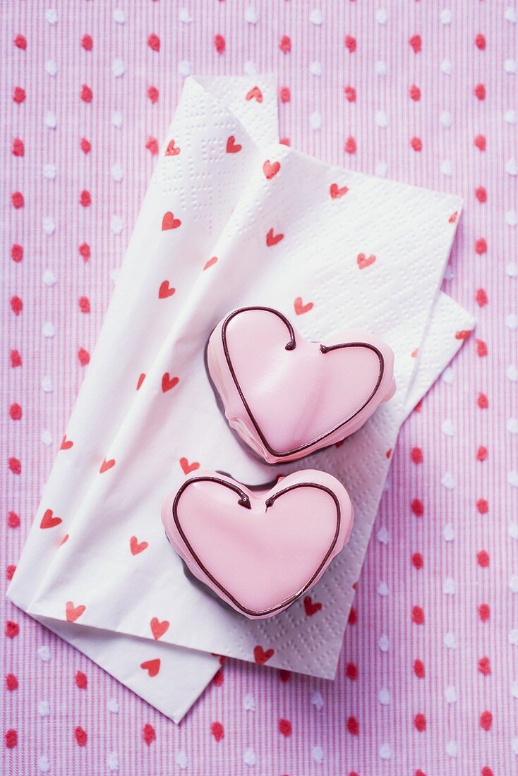 Two pink heart-shaped petit fours on paper napkin