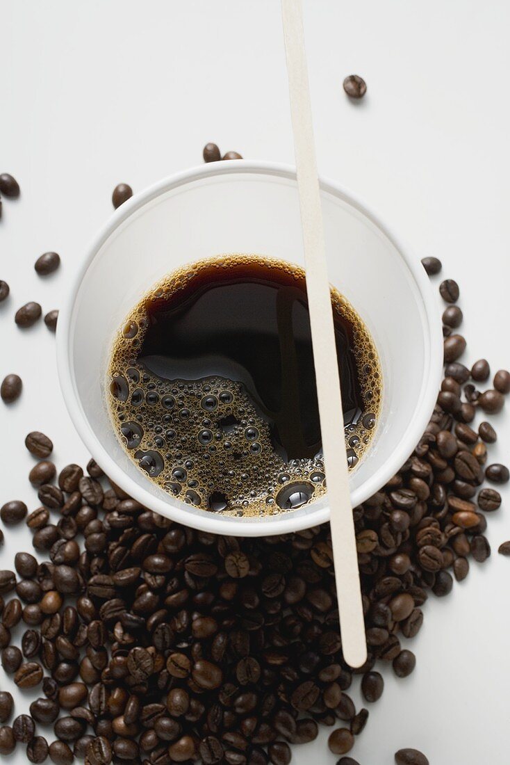 Schwarzer Kaffee im Plastikbecher zwischen Kaffebohnen