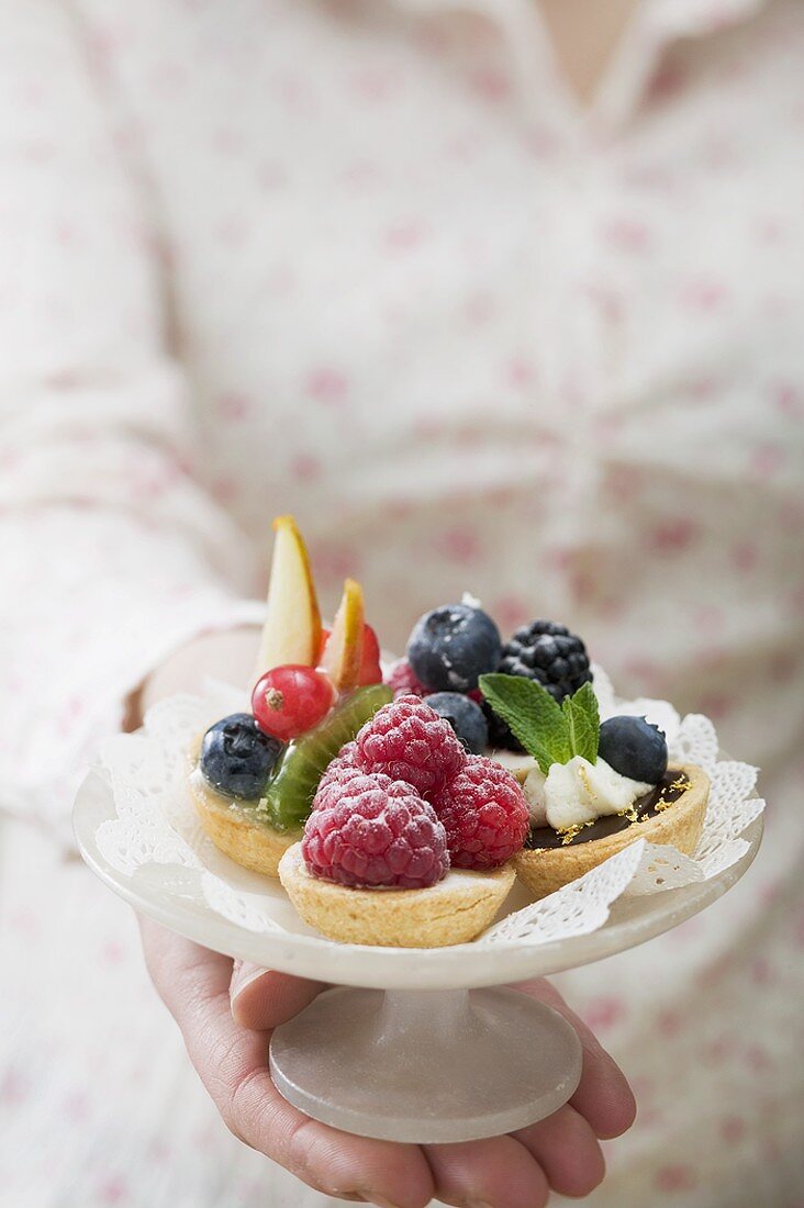 Woman holding berry tarts on cake stand