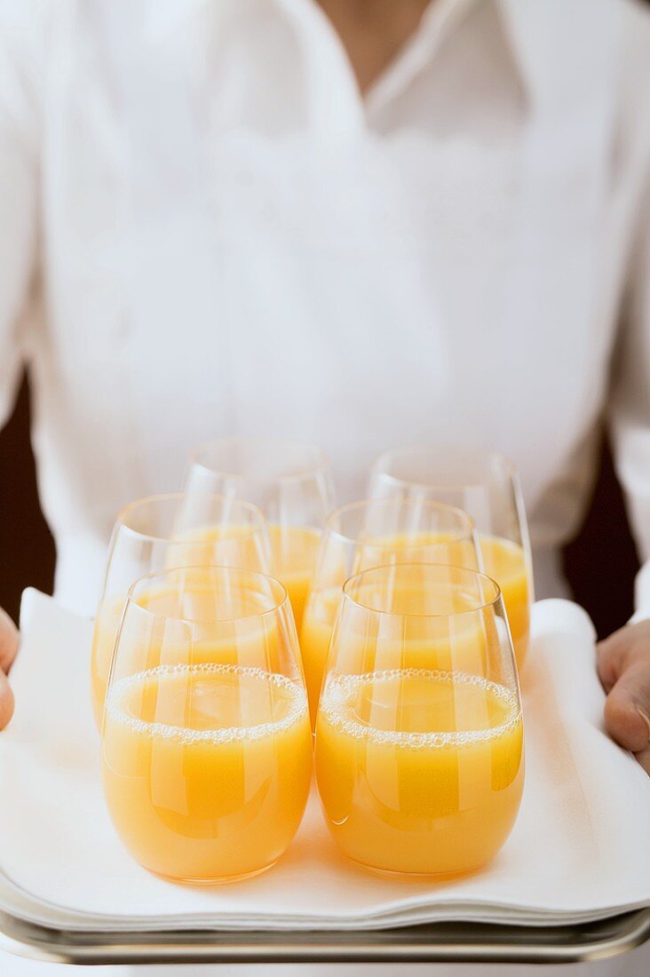 Zimmermädchen serviert mehrere Gläser Orangensaft auf Tablett