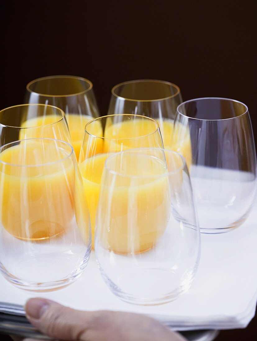 Several glasses of orange juice and empty glasses on tray