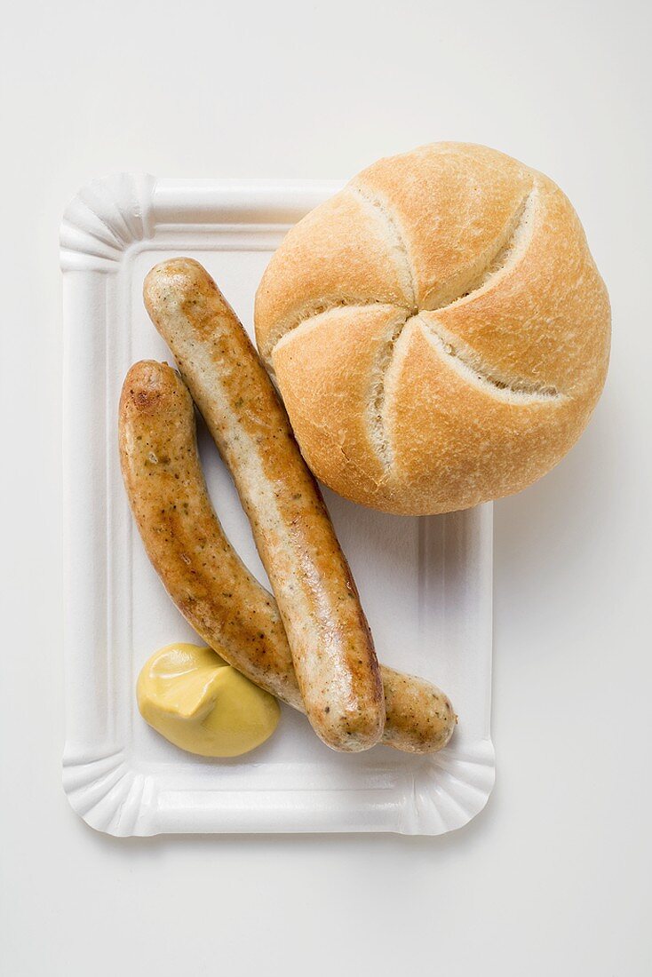 Bratwürstchen mit Senf und Brötchen auf Pappteller