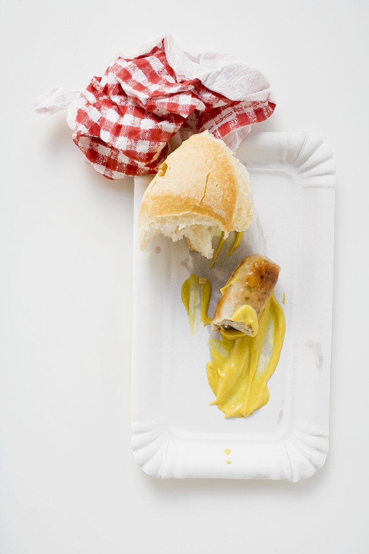 Remains of sausage with mustard & bread roll on paper plate