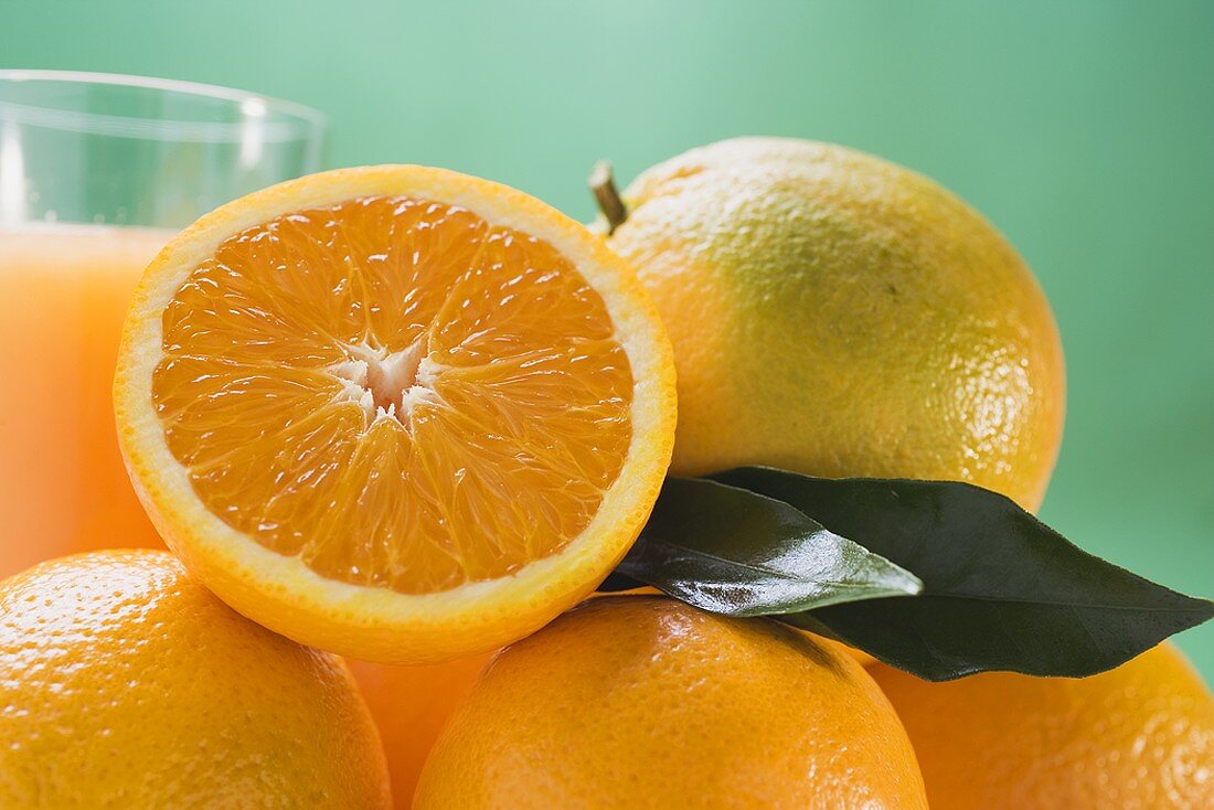 Several oranges, glass of orange juice in background