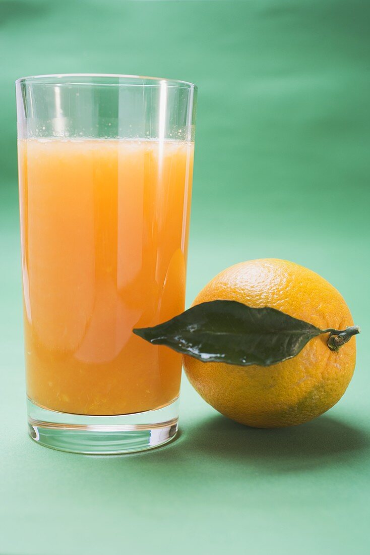 Glass of orange juice beside orange with leaf