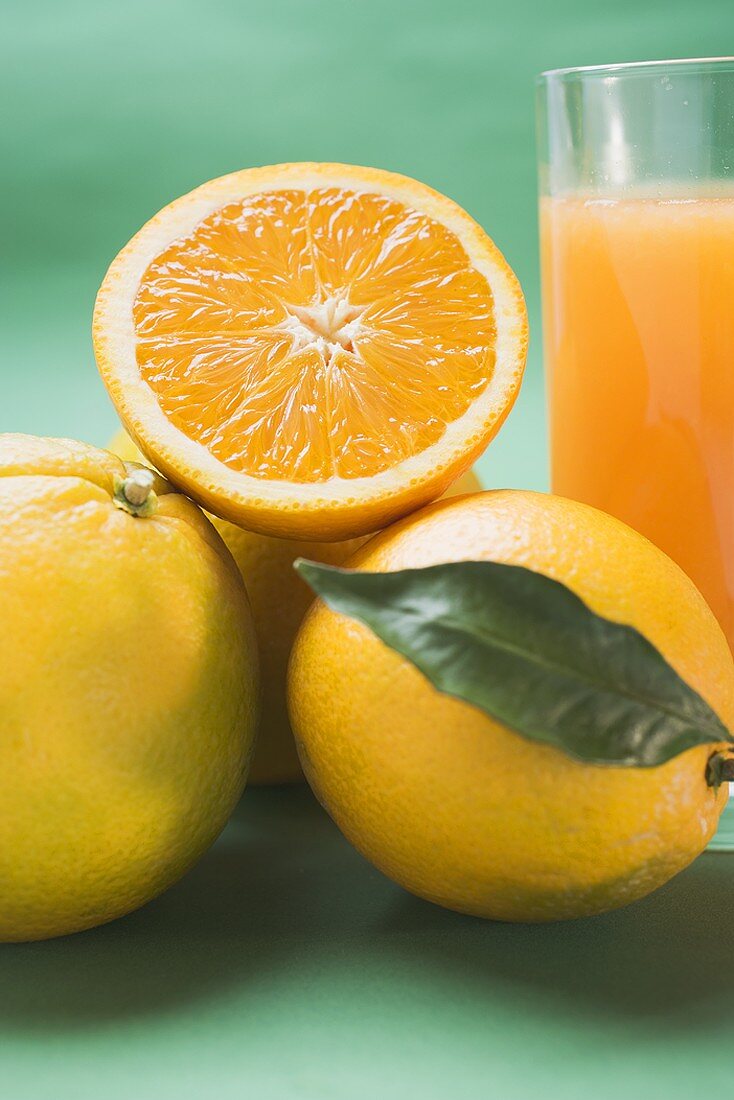 Glas Orangensaft und mehrere Orangen (Ausschnitt)