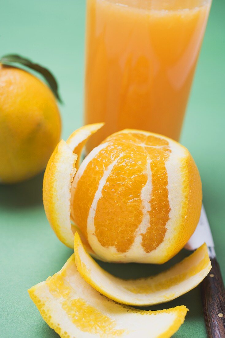 Peeled orange in front of glass of orange juice