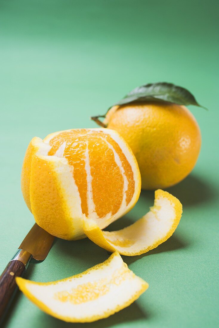 Two oranges, peeled and unpeeled, with knife