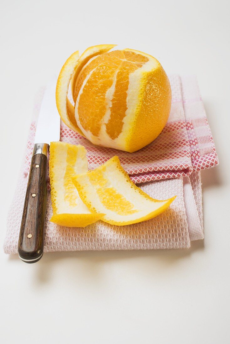 Geschälte Orange auf Geschirrtuch mit Messer