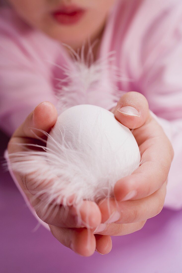 Child holding a white egg with feathers