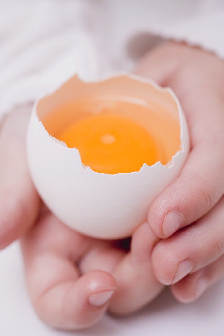Kinderhände halten aufgeschlagenes rohes Ei