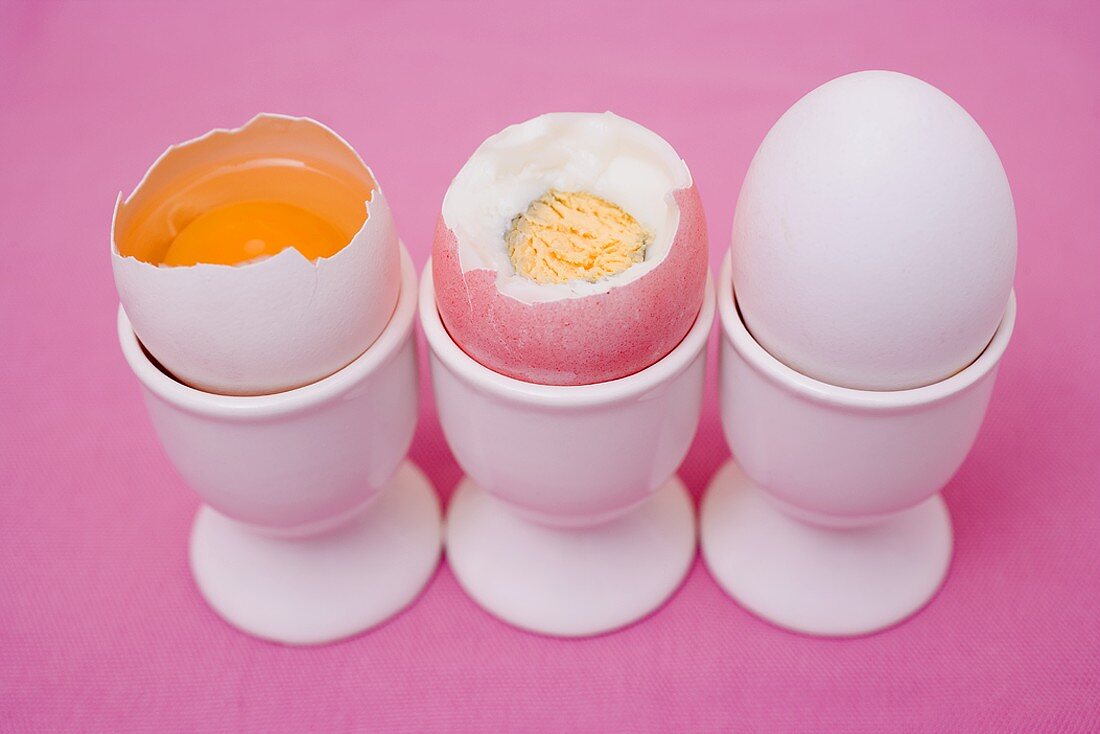 Drei Eier in Eierbechern (aufgeschlagen, roh, gekocht, ganz)