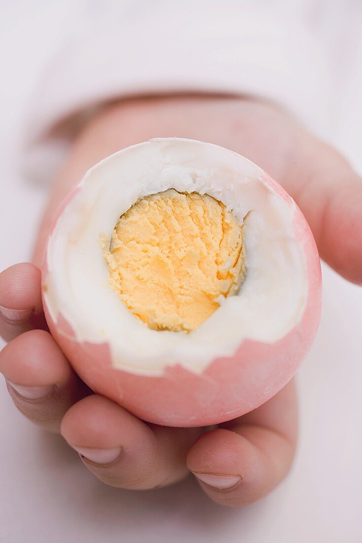 Child's hands holding coloured boiled egg with top cut off