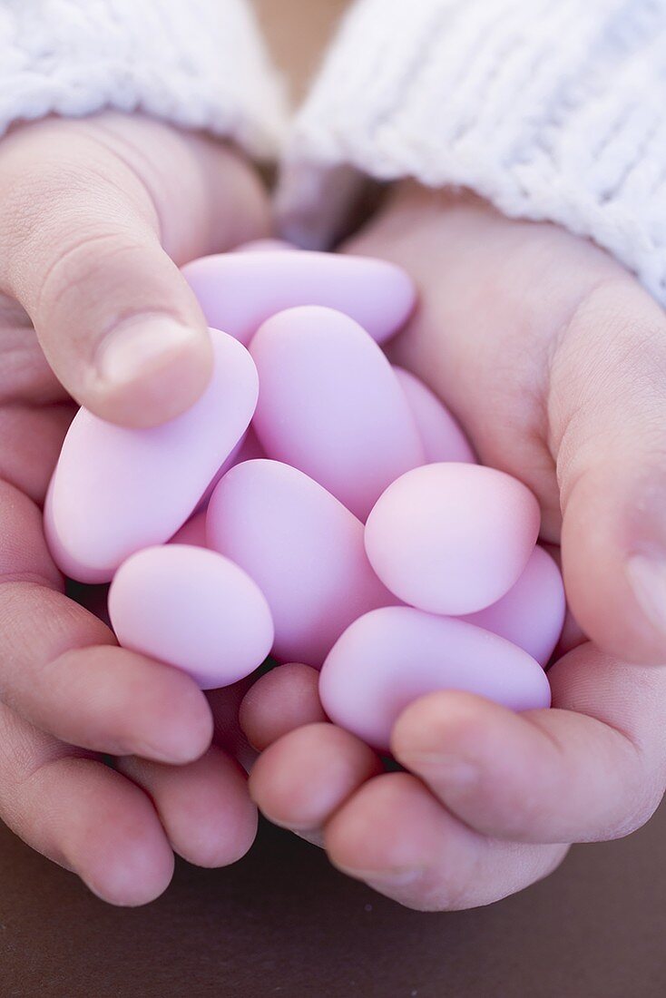 Kinderhände halten Mandeln mit rosa Zuckerglasur