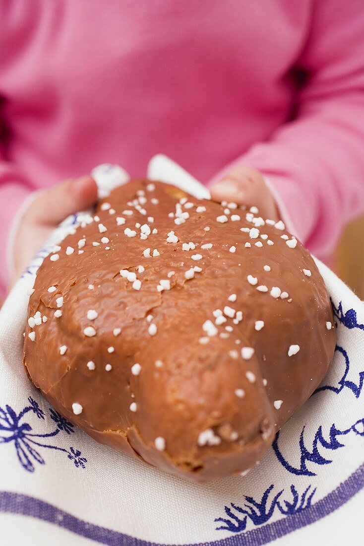 Child holding Easter cake with chocolate icing & pearl sugar