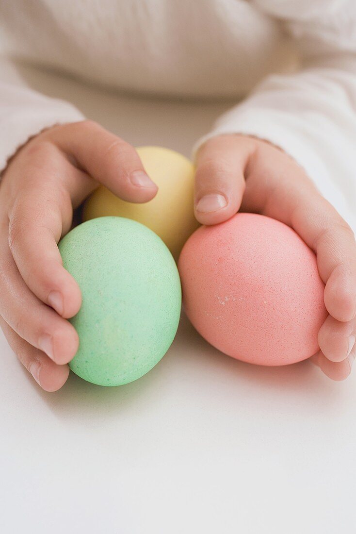 Kinderhände halten drei gefärbte Eier
