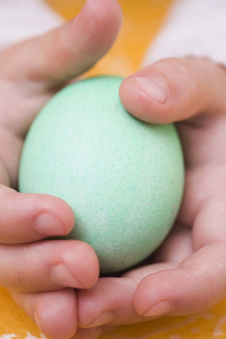 Kinderhände halten grün gefärbtes Ei
