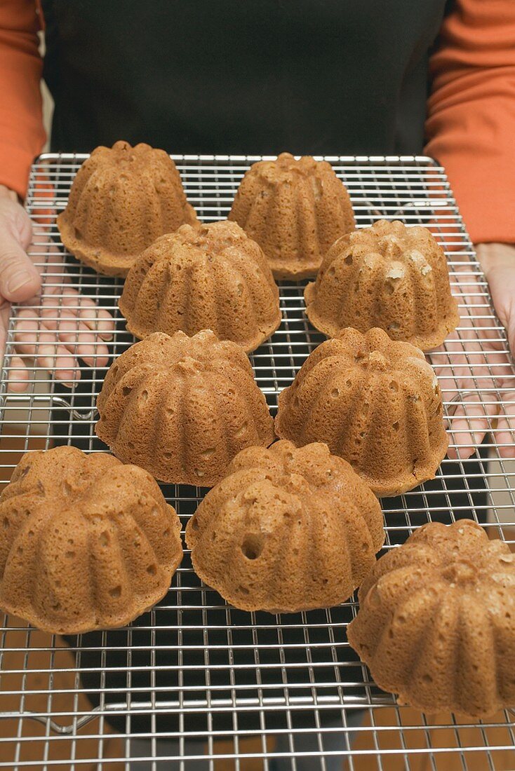 Hands holding freshly baked cakes on cake rack