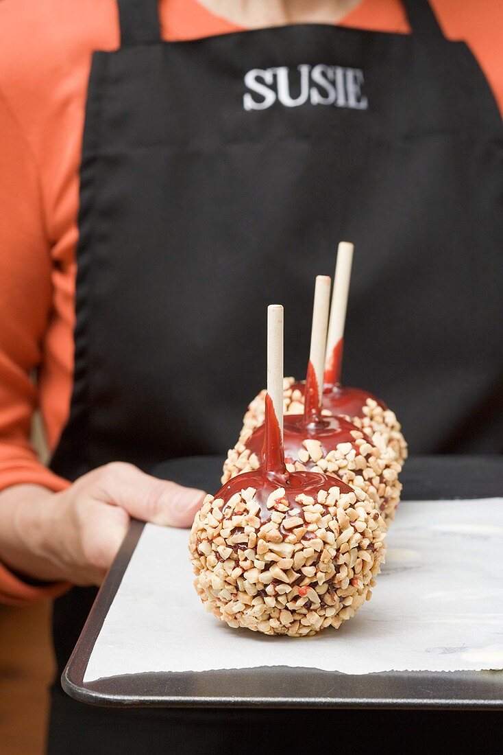 Woman holding a tray of toffee apples with chopped nuts