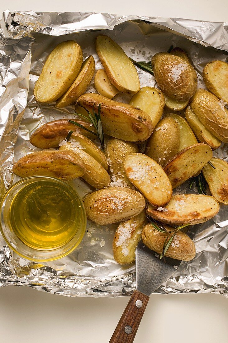 Rosemary potatoes on aluminium foil with spatula & olive oil