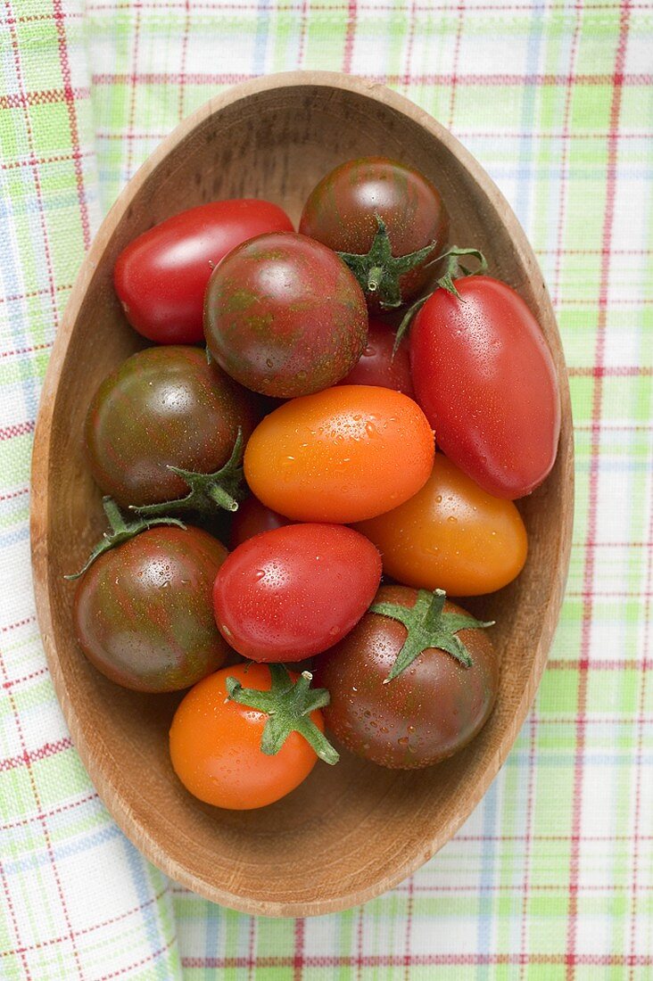 Different types of tomatoes in wooden dish (overhead view)
