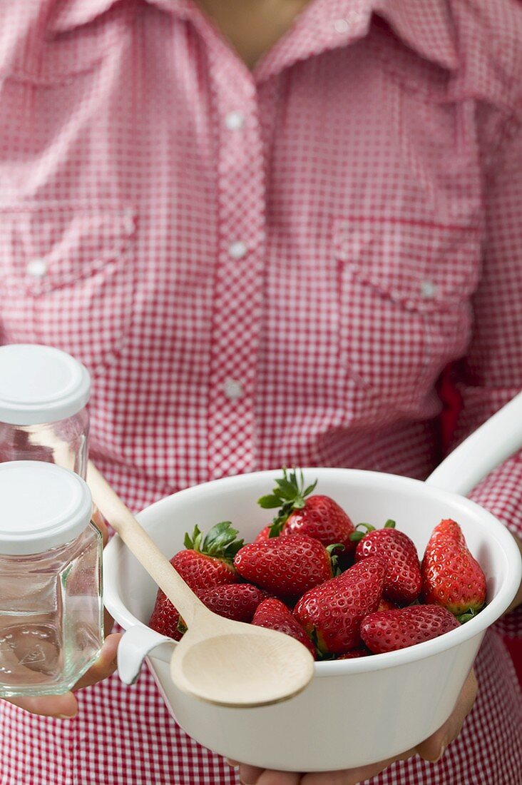 Woman holding strainer full of strawberries, jam jars, spoon