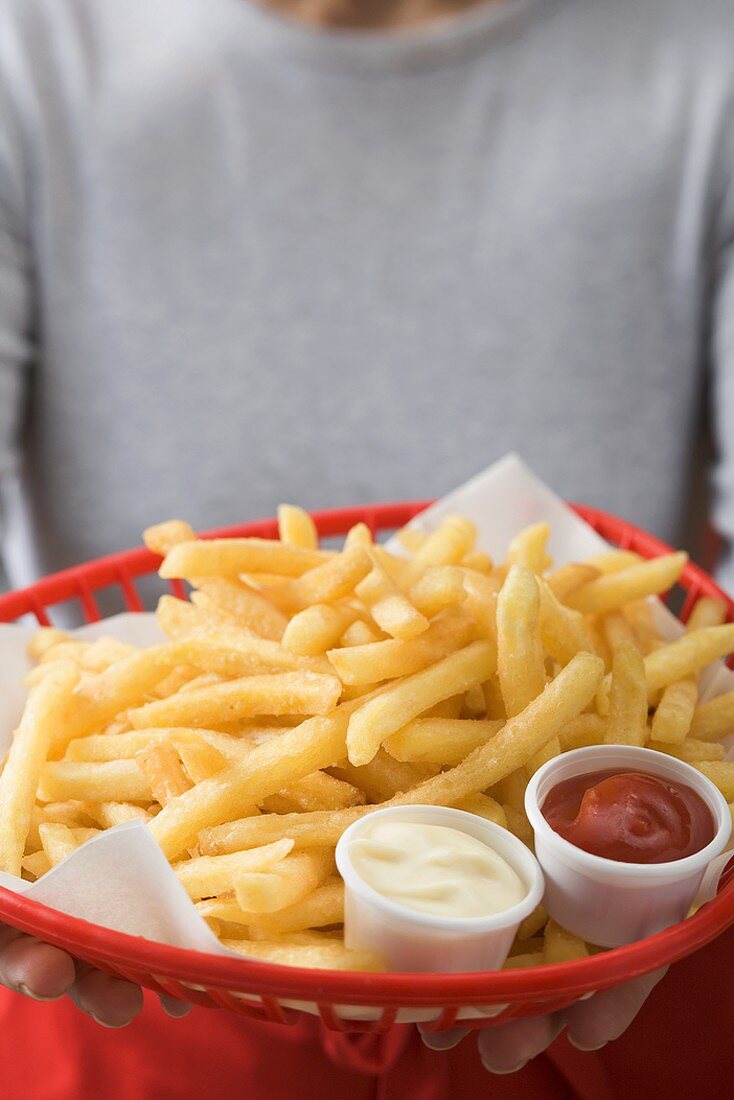 Frau hält Korb mit Pommes frites, Ketchup und Mayonnaise