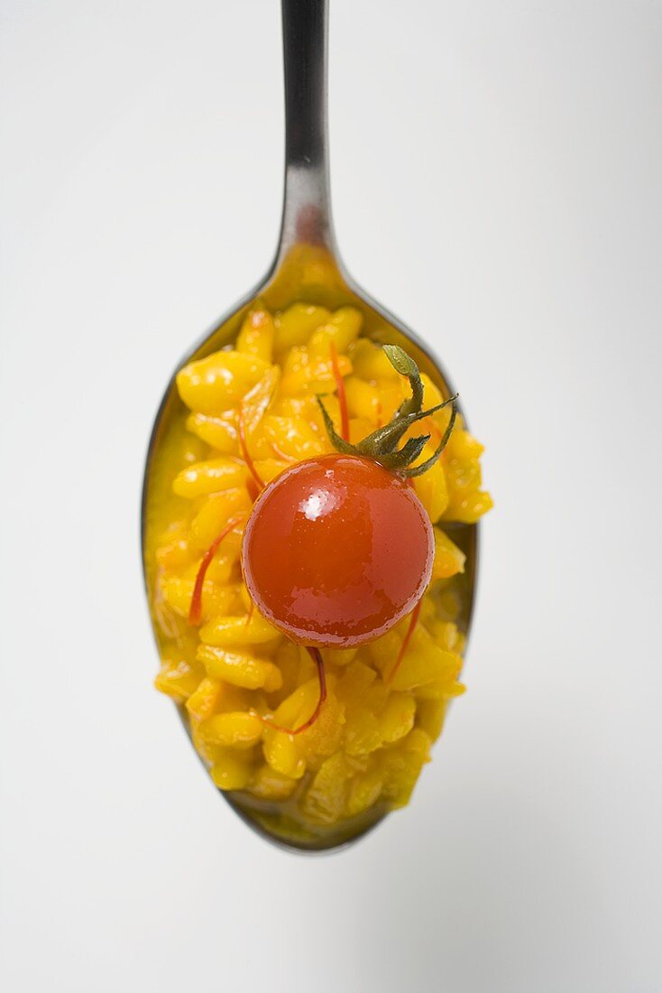 A spoonful of saffron risotto with cherry tomato (overhead)