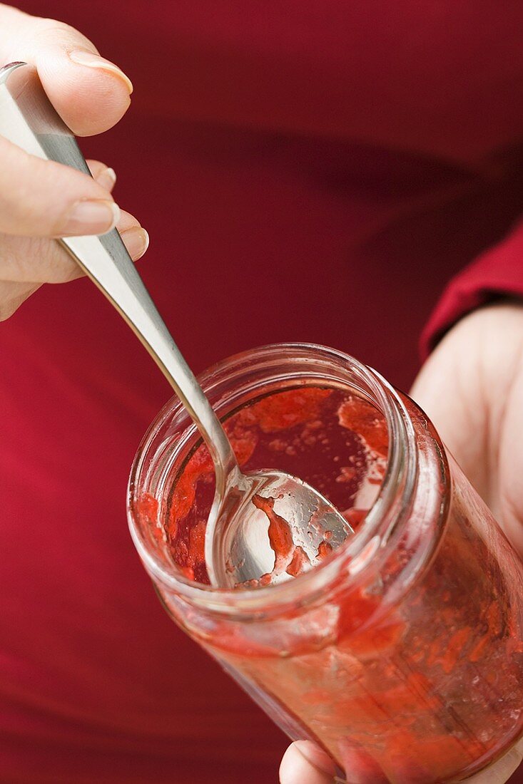 Frau hält Glas mit Resten von Erdbeermarmelade