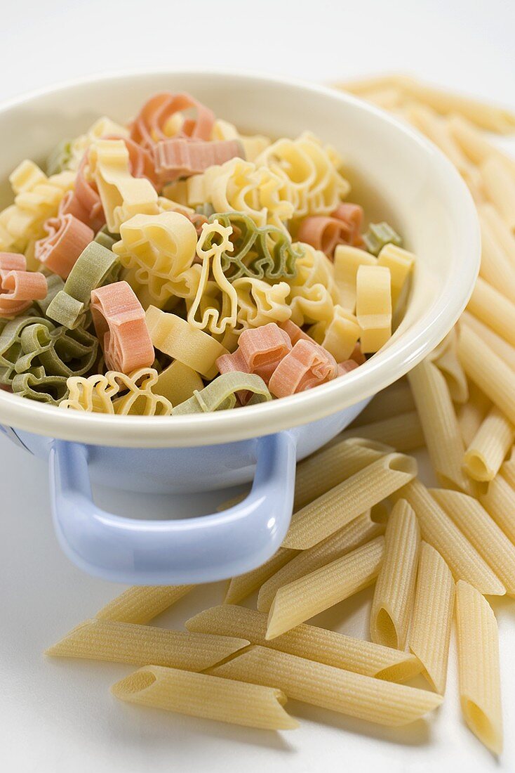 Coloured pasta in strainer, penne beside it