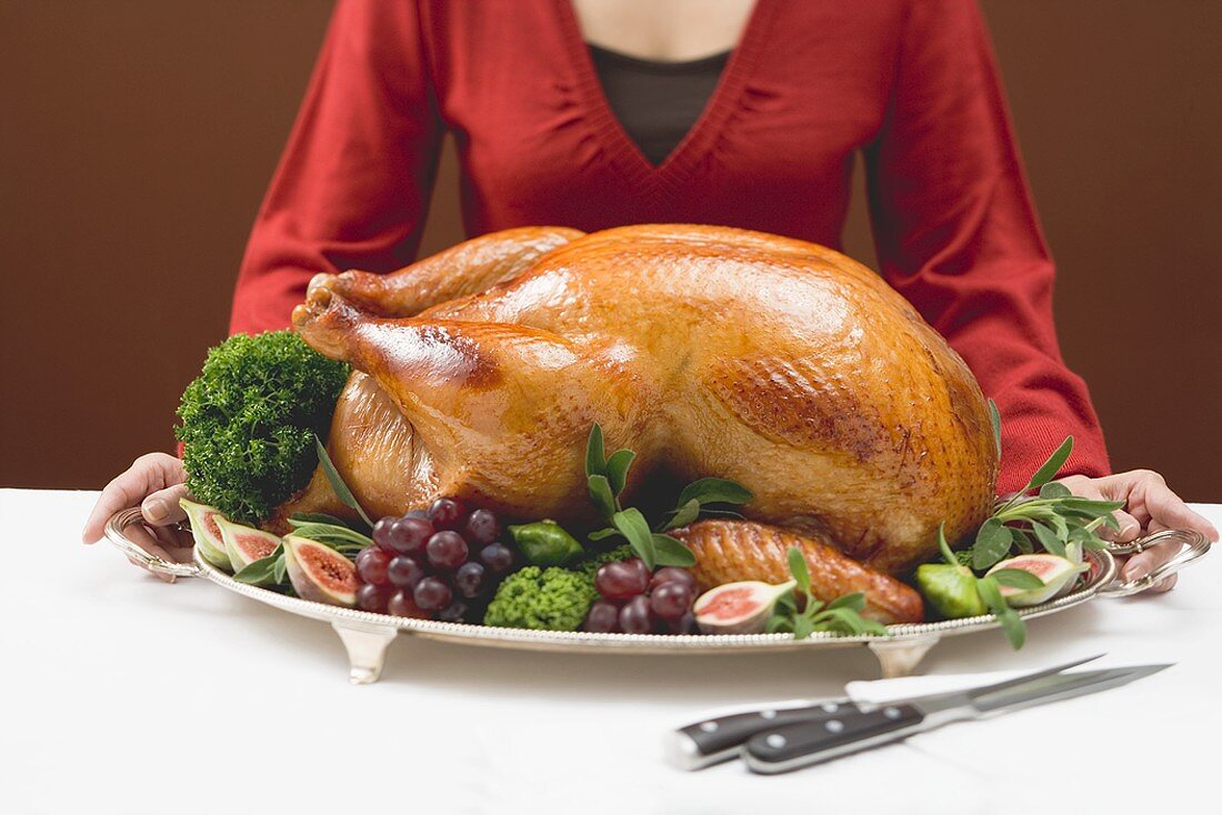 Woman holding platter with roast turkey and fruit