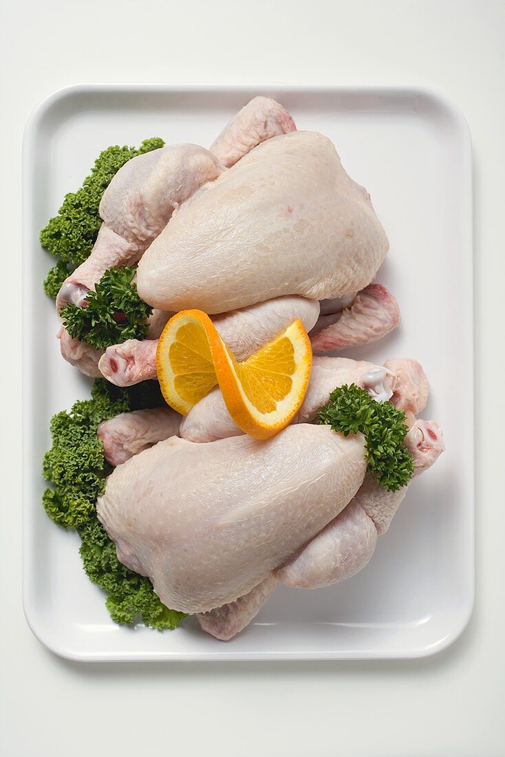 Two fresh chickens garnished with parsley and orange