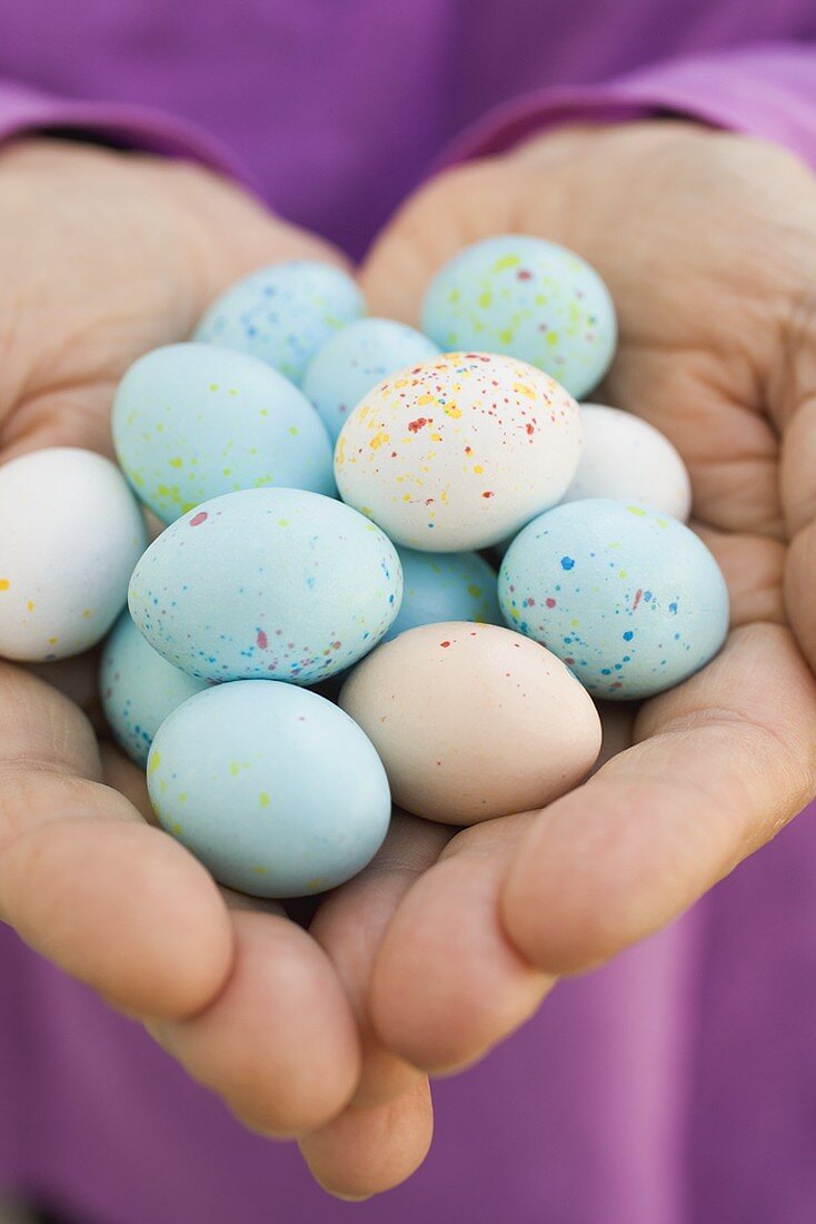 Hands holding chocolate eggs with pastel-coloured candy shells