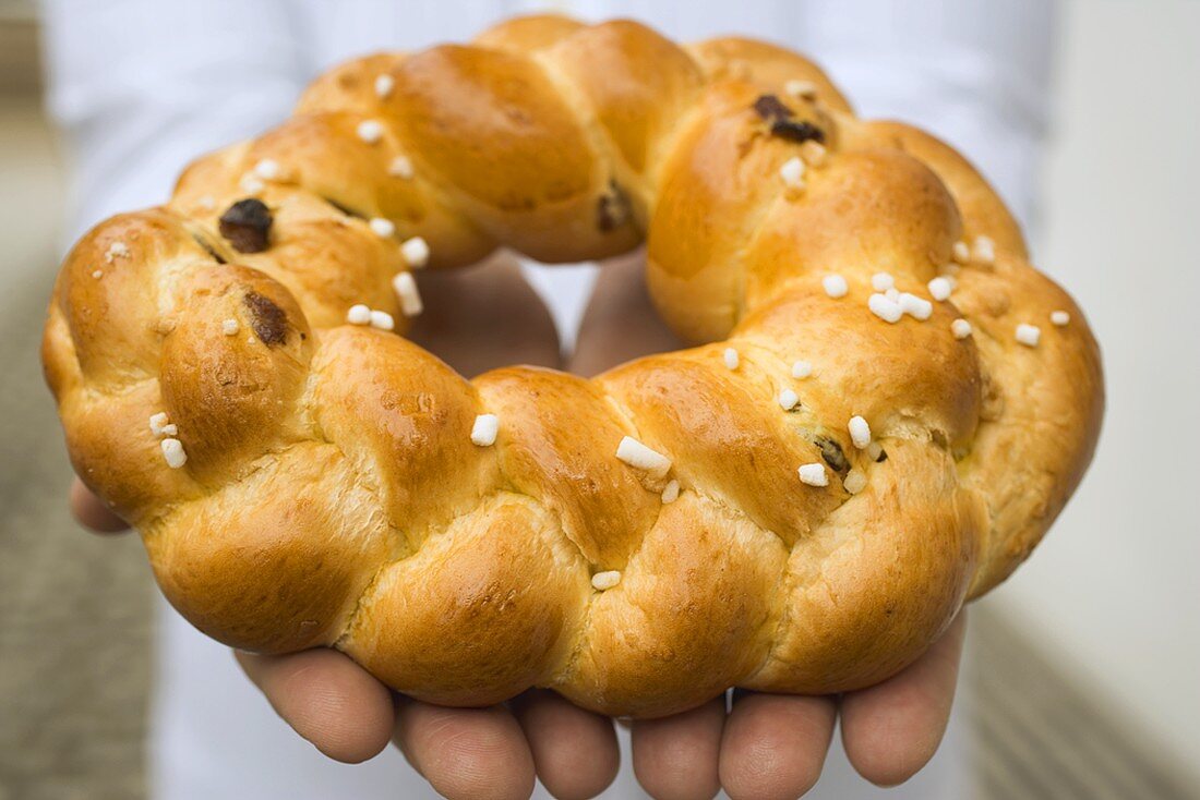 Hands holding plaited bread ring with pearl sugar (Easter)