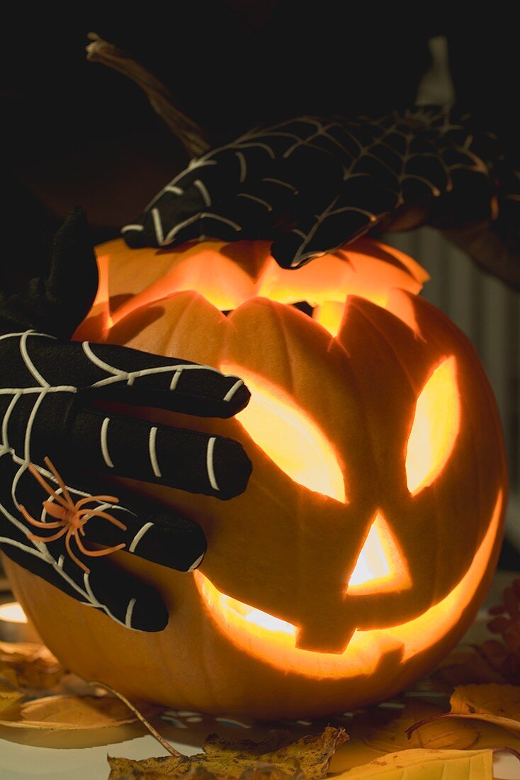 Hands in cobweb gloves holding pumpkin lantern