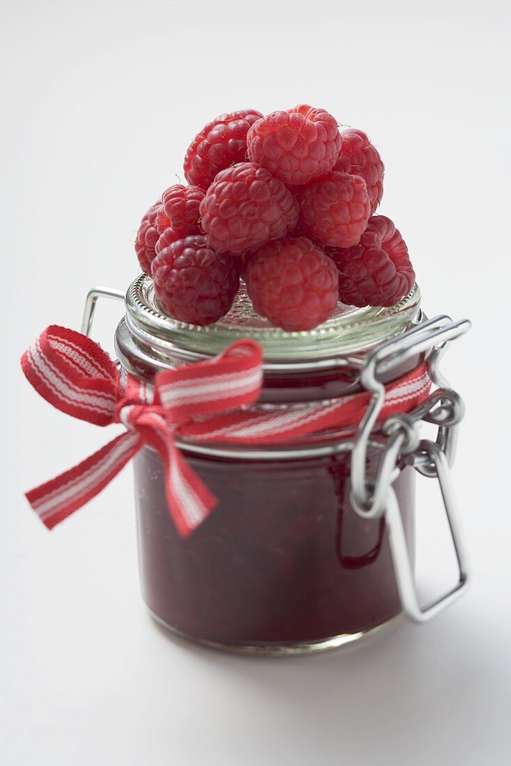 Jar of raspberry jam, fresh raspberries on top of jar