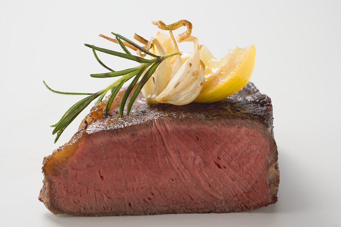 Beef steak, showing cut edge, with garlic, rosemary, lemon